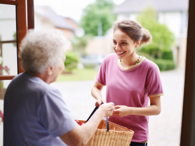 Image d'illustration montrant la référente de maison rendant visite à une dame, elles sont sur le pas de la porte et la référente lui a amené quelques courses